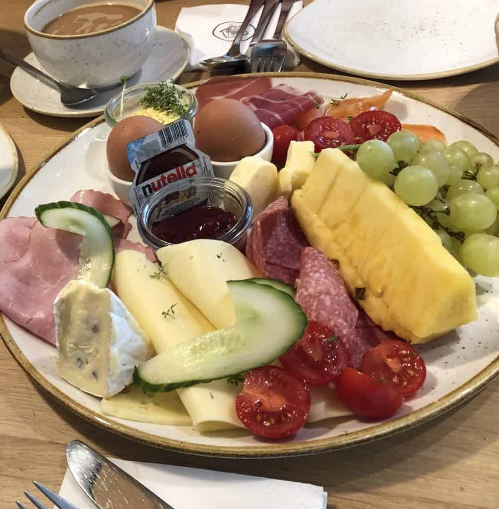 Frühstücksplatte mit Eier, Käse, Wurst, frischen Früchten und Nutella für einen perfekten Start in den Tag.