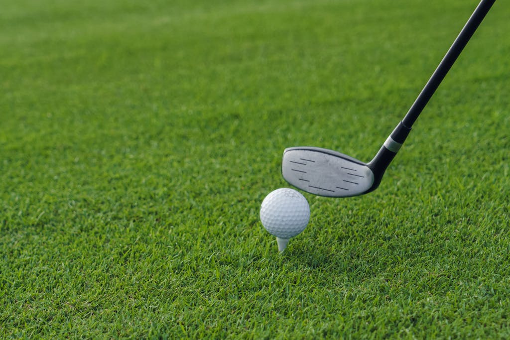 Golf club poised to hit a golf ball on a tee, set against a lush green grass background.
